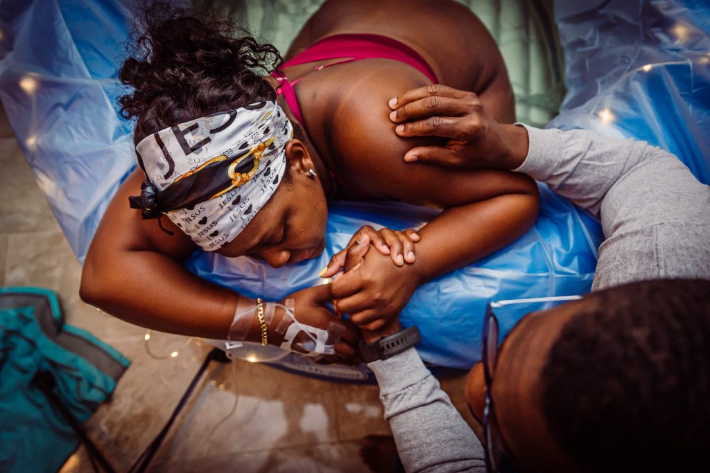 Partner holds hands and comforts a laboring mother during home water birth in South Florida. Birth photography by Martha Love.