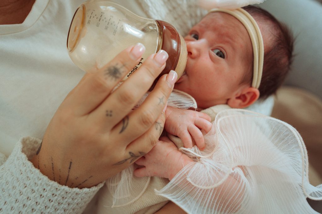 Newborn at home drinking from a bottle, being held by her mother