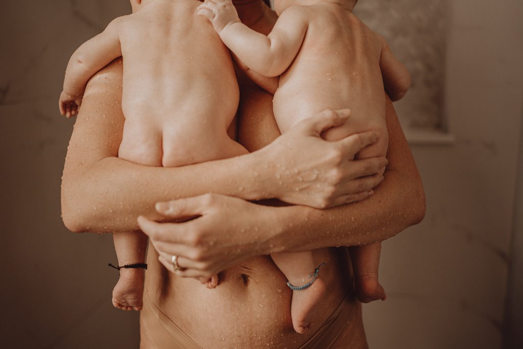 Mother holding newborn twins in the shower.