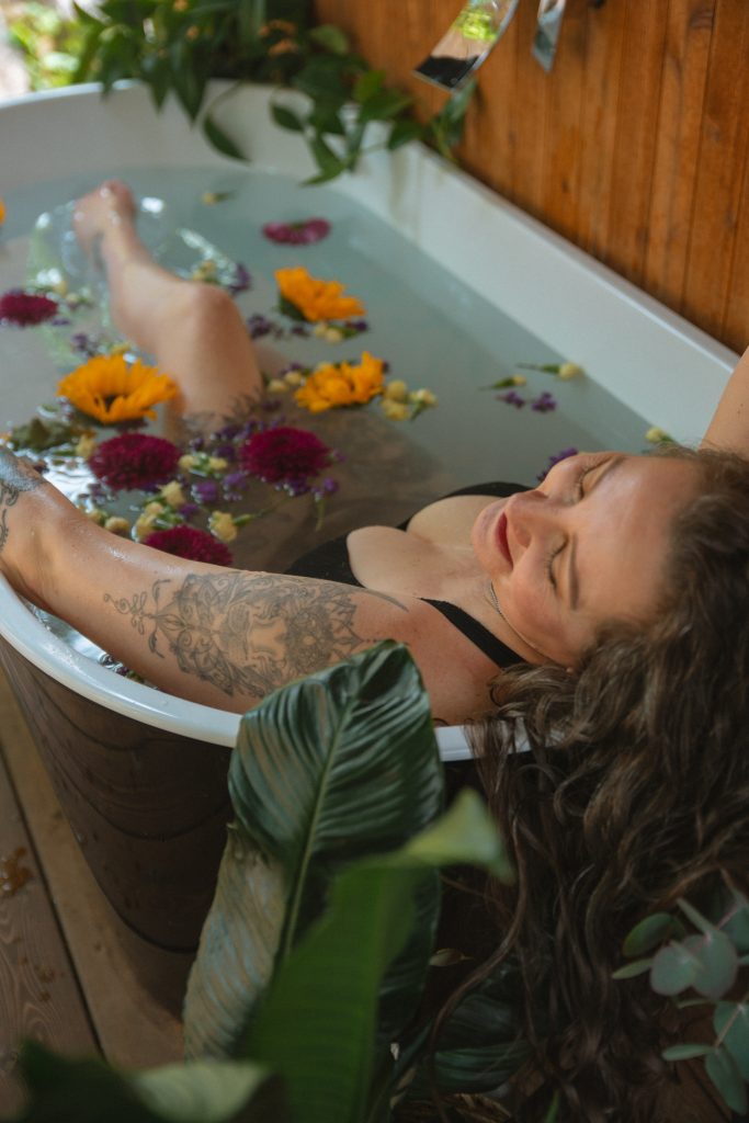 Woman in an outdoor bathtub surrounded by flowers, basking.