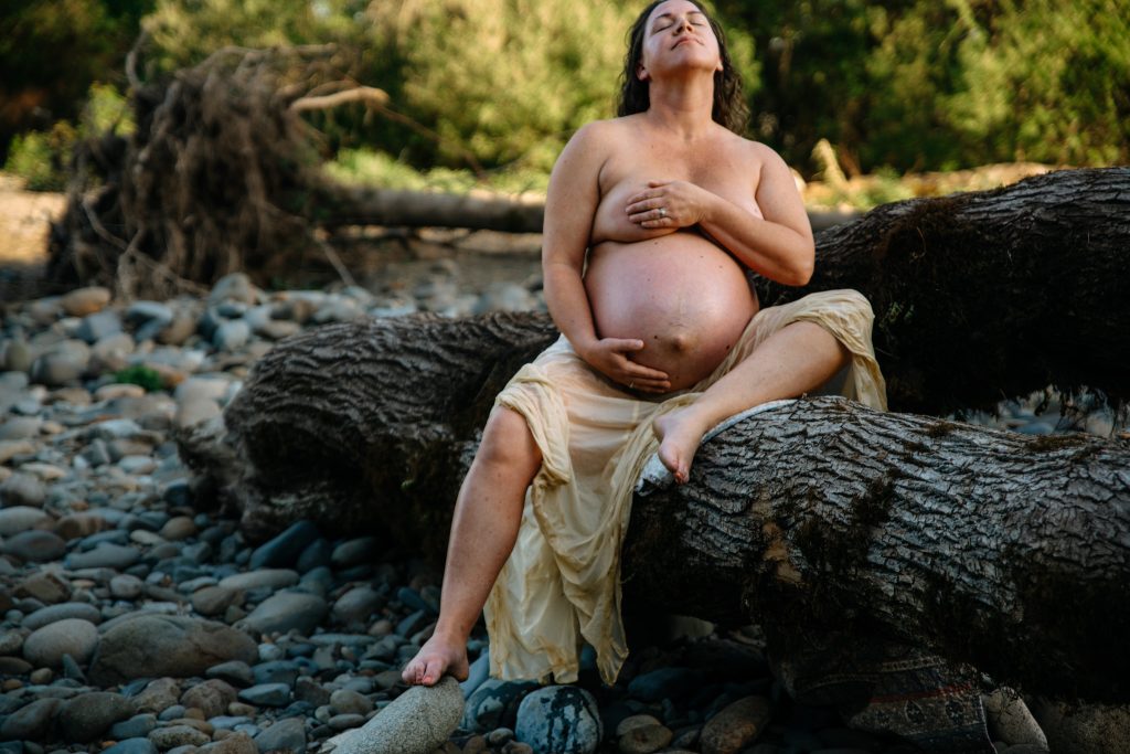 Pregnant woman sitting on a tree, connecting to herself, her baby, and nature.